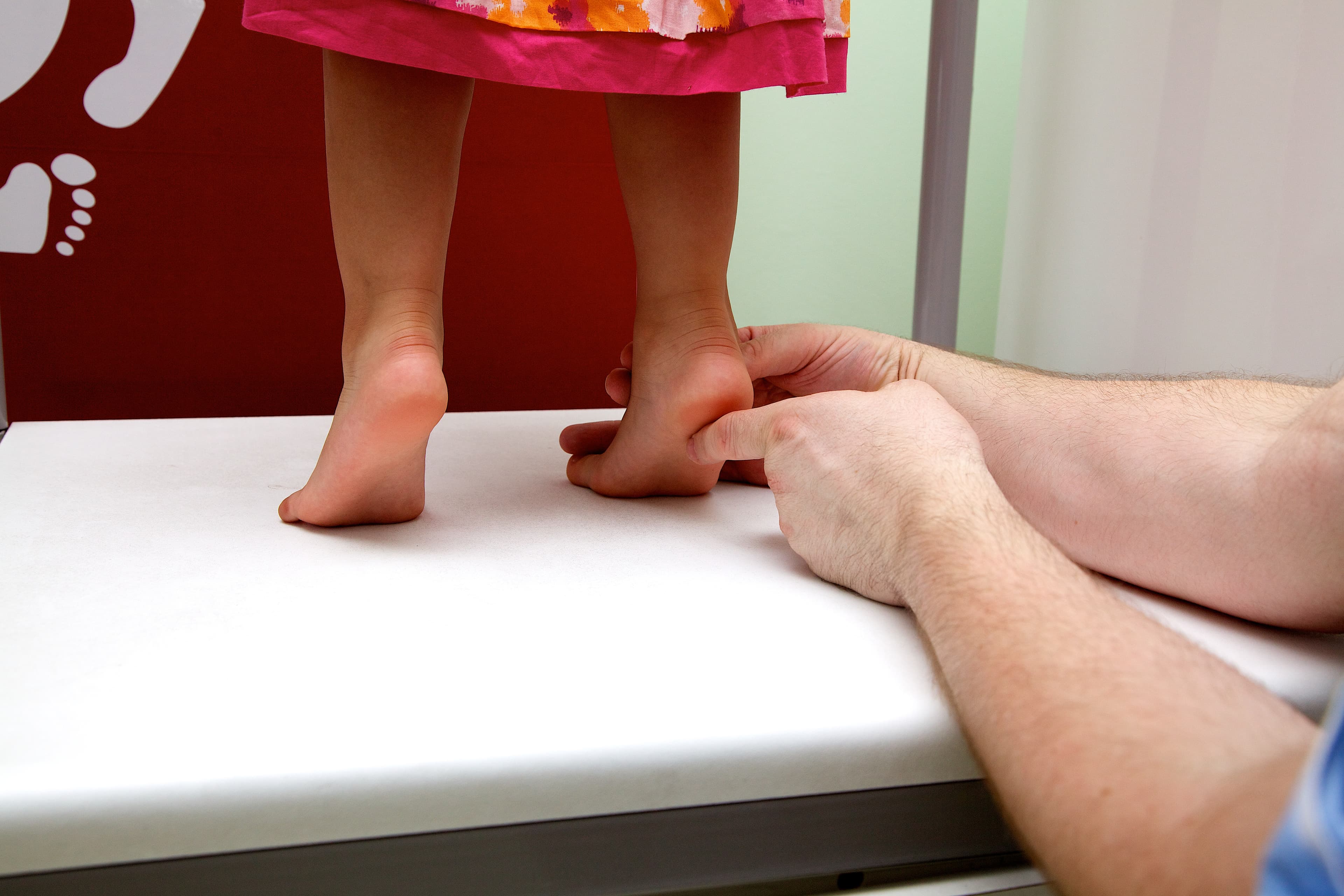 Orthopedic specialist examining a young child's bare feet and heels on a white medical platform.