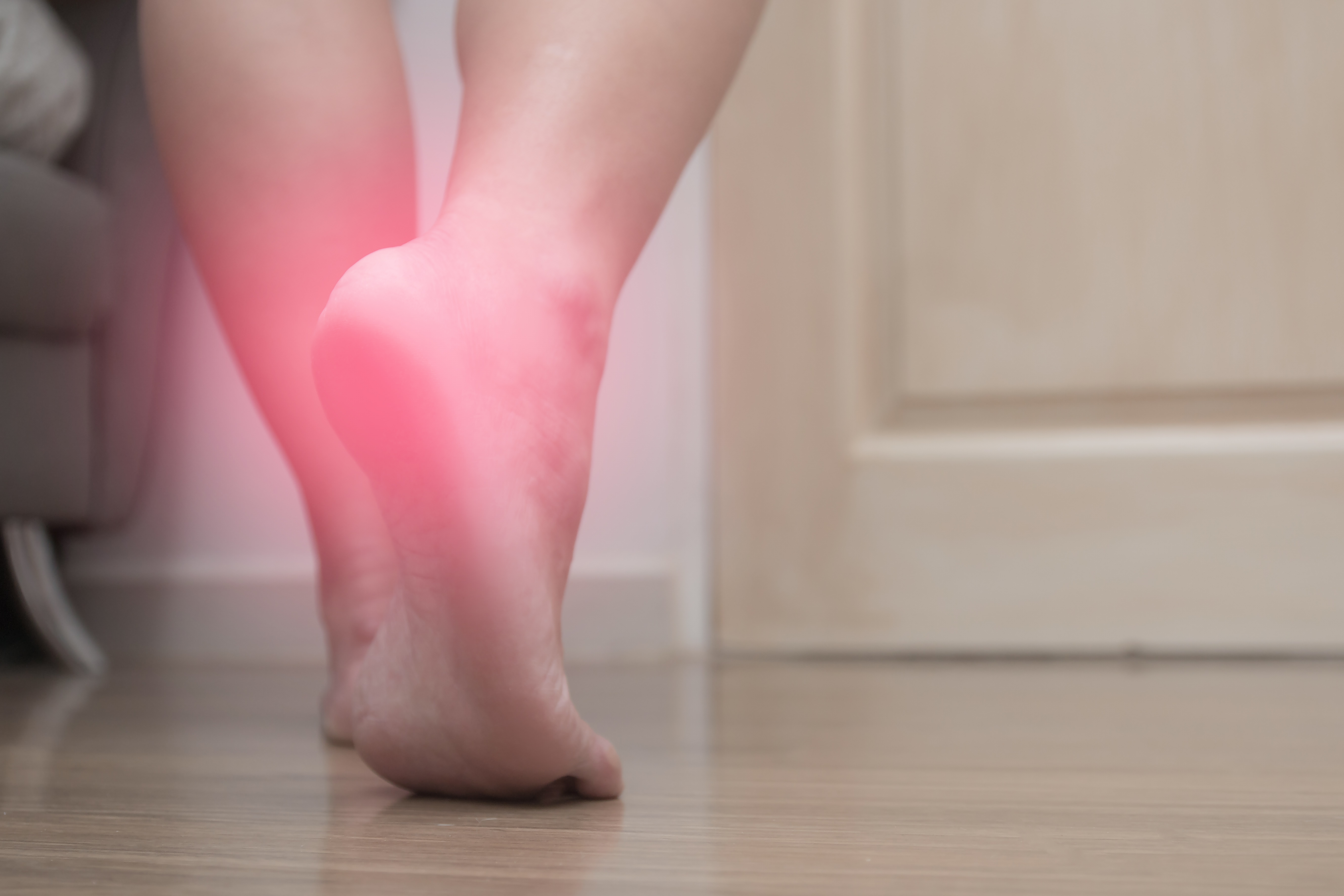 A person's bare foot with a red glow on the heel indicating pain or inflammation.